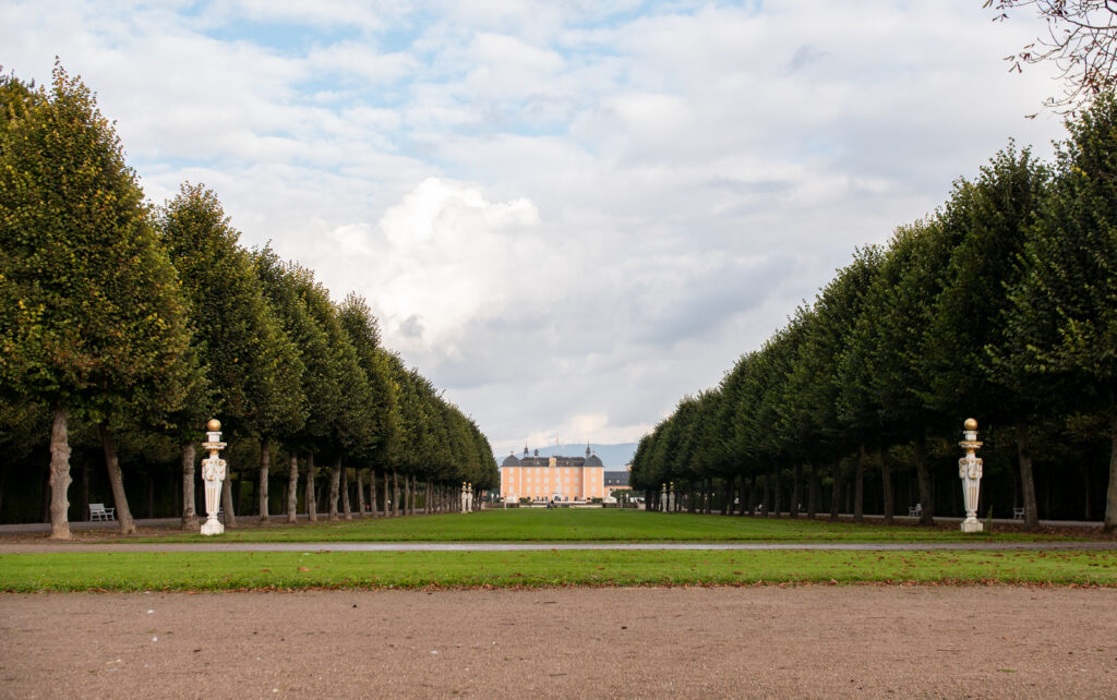 Schwetzingen Castle, view from the castle park. To the left and right of the park, historical columns with golden balls line the path.